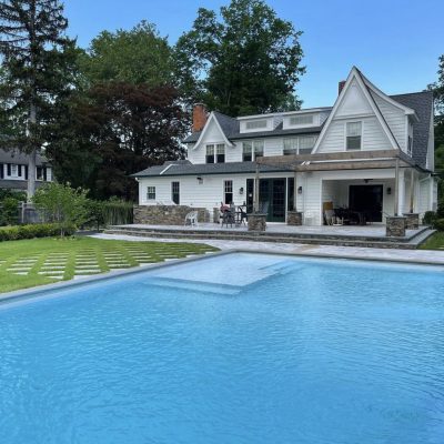 A large backyard pool beside a white house showcases Caswell Beach Tile and Sandy Point Floor in Long Island.