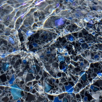 Sunlight sparkles on Midnight Opal mosaic tiles in a pool, creating a vibrant, reflective surface.