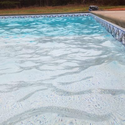 Close-up of a clear blue NY pool bordered by concrete deck and featuring Caswell Beach Tile flooring.