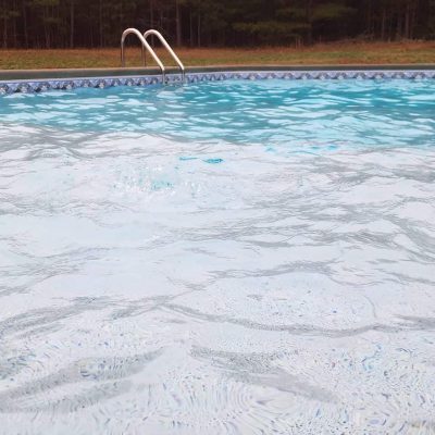Close-up of a pool with metal ladder, featuring Caswell Beach Tile flooring in Long Island & Queens, NY.