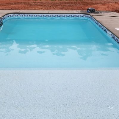 A Caswell Beach Tile/Sandy Point Floor pool in NY shows concrete, red dirt, and supplies nearby.