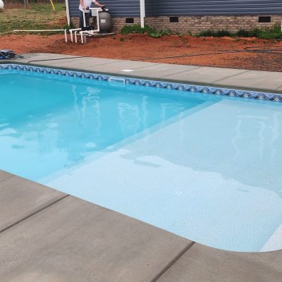 A rectangular in-ground pool by a home features sandy-toned Caswell Beach Tile near Long Island & Queens.