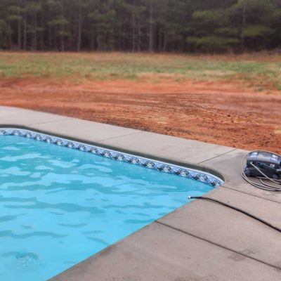 Caswell Beach Tile and Sandy Point Floor highlight a pool deck beside a grassy field in Long Island, NY.