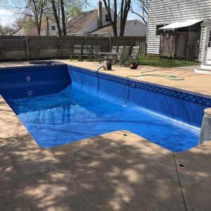 An empty backyard pool with a Blue Trinidad Tile Jamaica Floor liner and patio in Long Island is shown.