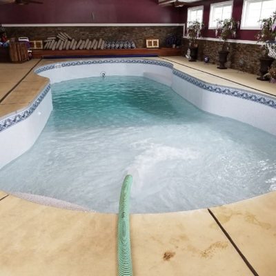 An indoor NY pool is being filled, showcasing Caswell Beach Tile and Sandy Point Floor in Long Island.