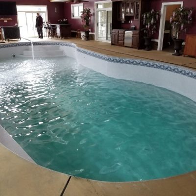 An indoor kidney-shaped pool room features Caswell Beach Tile and Sandy Point Floor for a modern look.