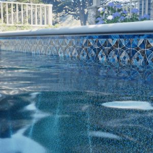 Close-up view of a backyard pool in NY featuring Horizon Tide Floor tile, water reflections, and pool supplies.