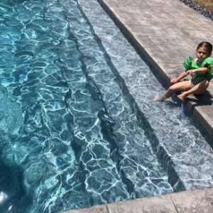 A child in a green shirt relaxes by the pool in NY, enjoying sun with Island Granite All Over Pattern.