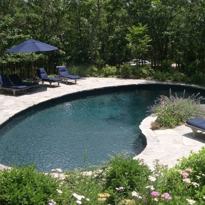 A kidney-shaped solid black pool with lounge chairs and an umbrella, perfect for Long Island relaxation.