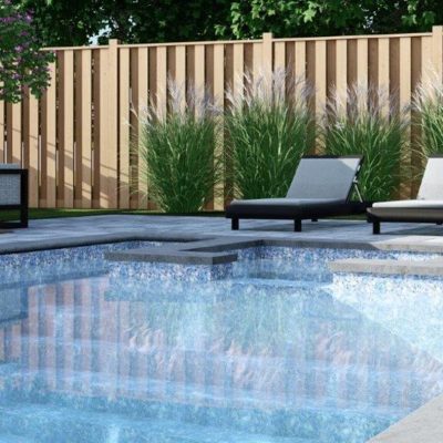 Three Moonstone Bay lounge chairs sit by a NY backyard pool, surrounded by tall grass and wood fencing.