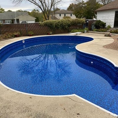 A backyard swimming pool with curved edges and blue water features Royal Island Tile Sea Storm Floor.