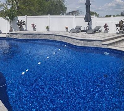 Curved blue pool with Royal Island Tile, Sea Storm Floor, stone deck, and lounge chairs in Long Island.