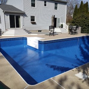 Empty in-ground pool with Santa Maria Tile Blue Cove floor by a light gray NY house; pool supplies nearby.