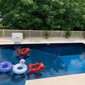 A Shelter Cove All Over Pattern float drifts in a backyard pool with vibrant summer supplies nearby.