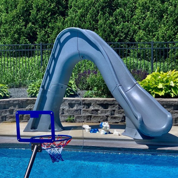 A Tidal Wave Deck Mounted Pool Slide sits next to a swimming pool in a lush, plant-filled backyard.