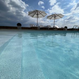 Caswell Beach Tile surrounds the pool with loungers and umbrellas at a Long Island, NY, pool supplies spot.