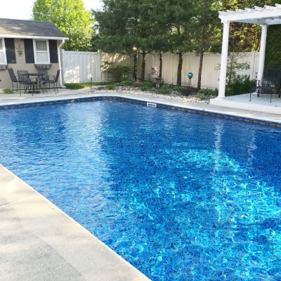 A clear blue pool with patio seating features Sandy Cay Tile and Runaway Bay Floor in Long Island, NY.