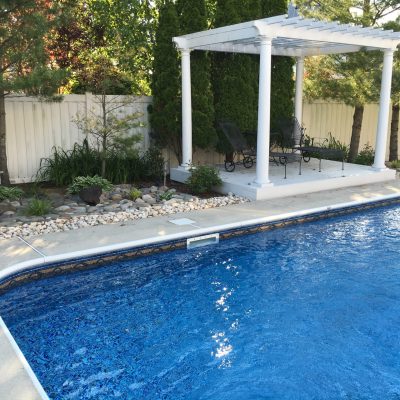 A NY backyard pool with Sandy Cay Tile, Runaway Bay Floor, clear blue water, pergola, and lush garden.