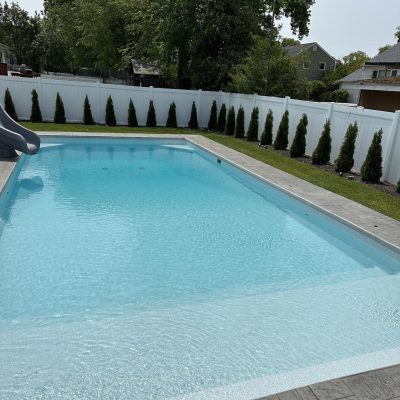 A backyard in Long Island with Caswell Beach Tile and Sandy Point Floor surrounds a sparkling blue pool.