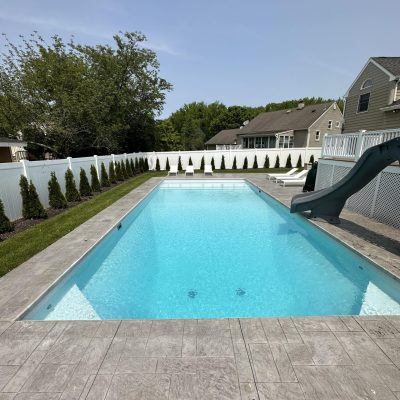 Backyard pool with slide, trees, and white fence features Caswell Beach Tile in Long Island, NY.