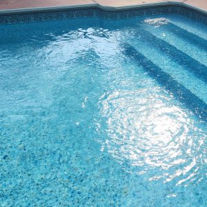 Sunlight sparkles on a clear blue pool with Aster Tile and Ocean Breeze Floor in Long Island, Queens.