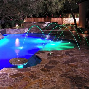 A night pool scene showcases Infinite WaterColors Laminar Jet RGBW LED lighting and a stone patio.